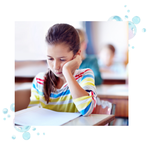 A young girl sitting at a desk in school looking at her notebook.